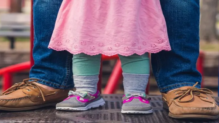 la foto mostra le gambe di una bambina in piedi fra le gambe del papà per rappresentare l'assistente all'infanzia