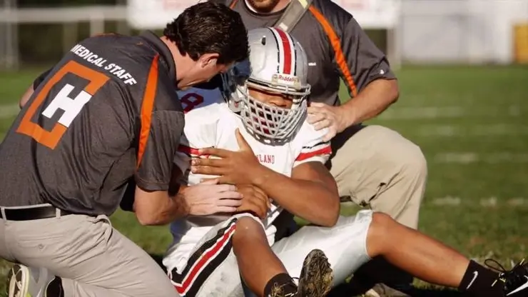 un giocatore di football americano seduto sul campi mentre il personale medico interviene